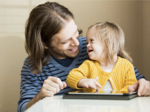 Father smiling at a laughing child using an AT device