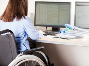 Secondary Transition Preparation - a woman in a wheelchair sits at a desk and works on a desktop computer