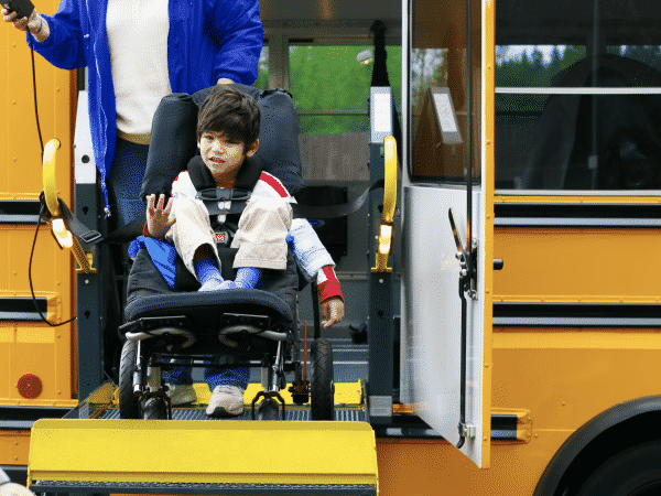 Young boy in wheelchair exiting bus with the help of a ramp