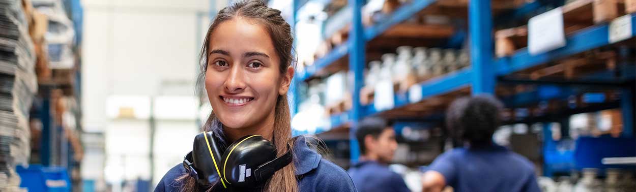 smiling young woman with hearing protectors in a warehouse with co-workers